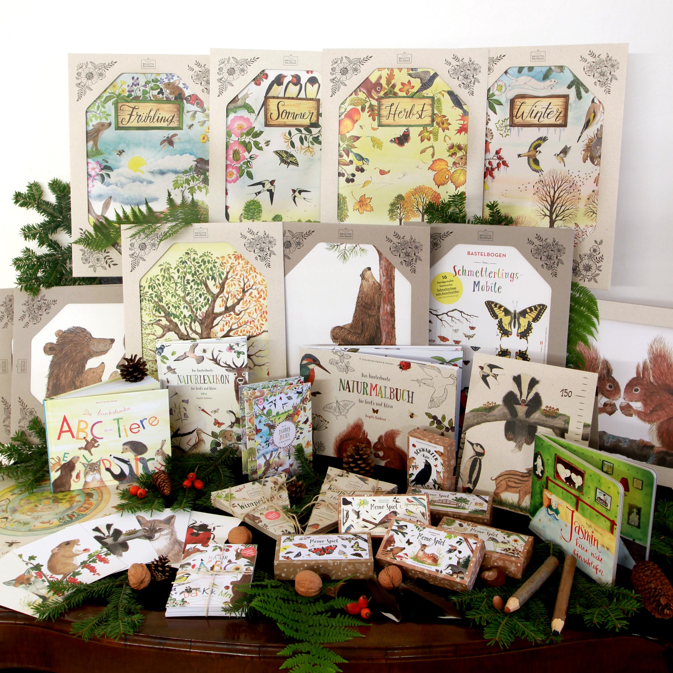 Spiele, Bilderbücher, Poster und Papeteriewaren. Prsäsentiert auf einem Holztisch mit Naturmaterialien dekoriert