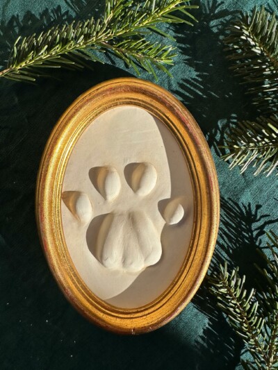 Gipsabguss einer Luchsspur, gerahmt in einem ovalen Holzrahmen mit Gold