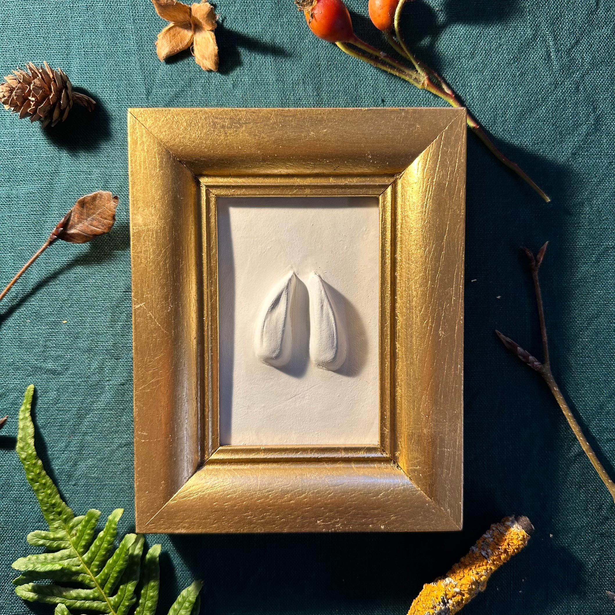 Gipsabguss einer Rehspur gerahmt in einem eckigen Goldrahmen aus Holz